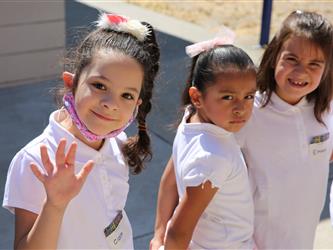 three elementary girls in uniform waving and smiling